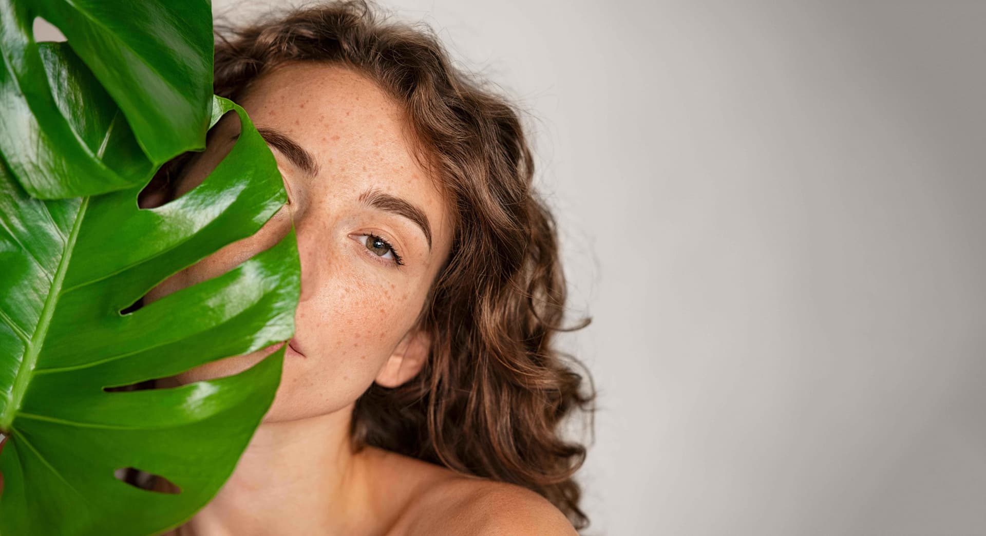 Frau mit strahlender Haut und Monstera Blatt - Aquafacial Behandlung